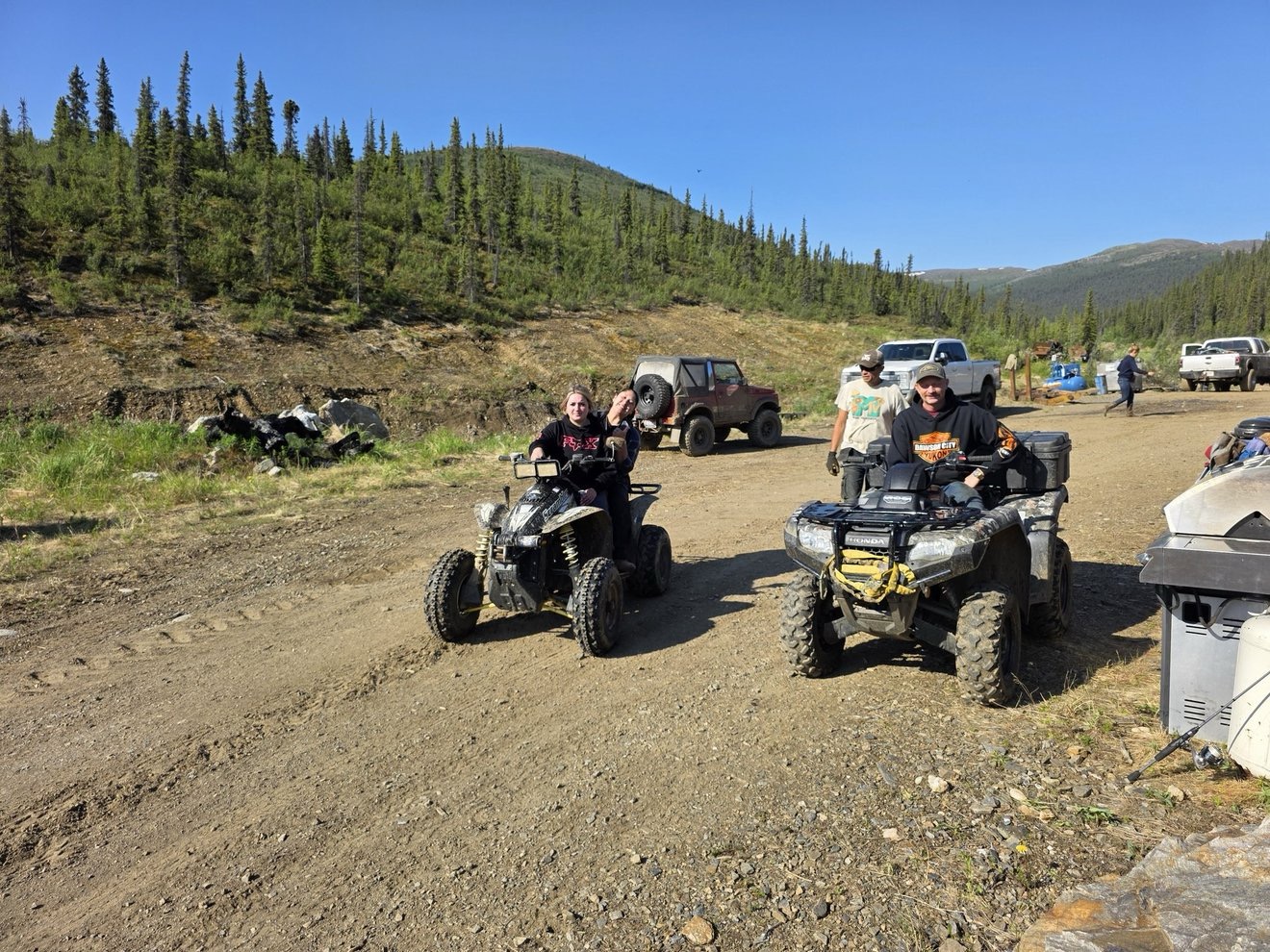 ATVs and crew members gathered on a dirt road at camp.