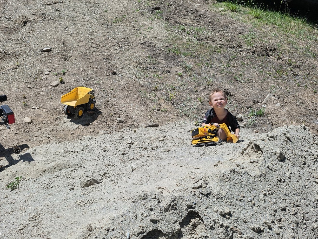 Child playing with toy trucks in sandy ground.