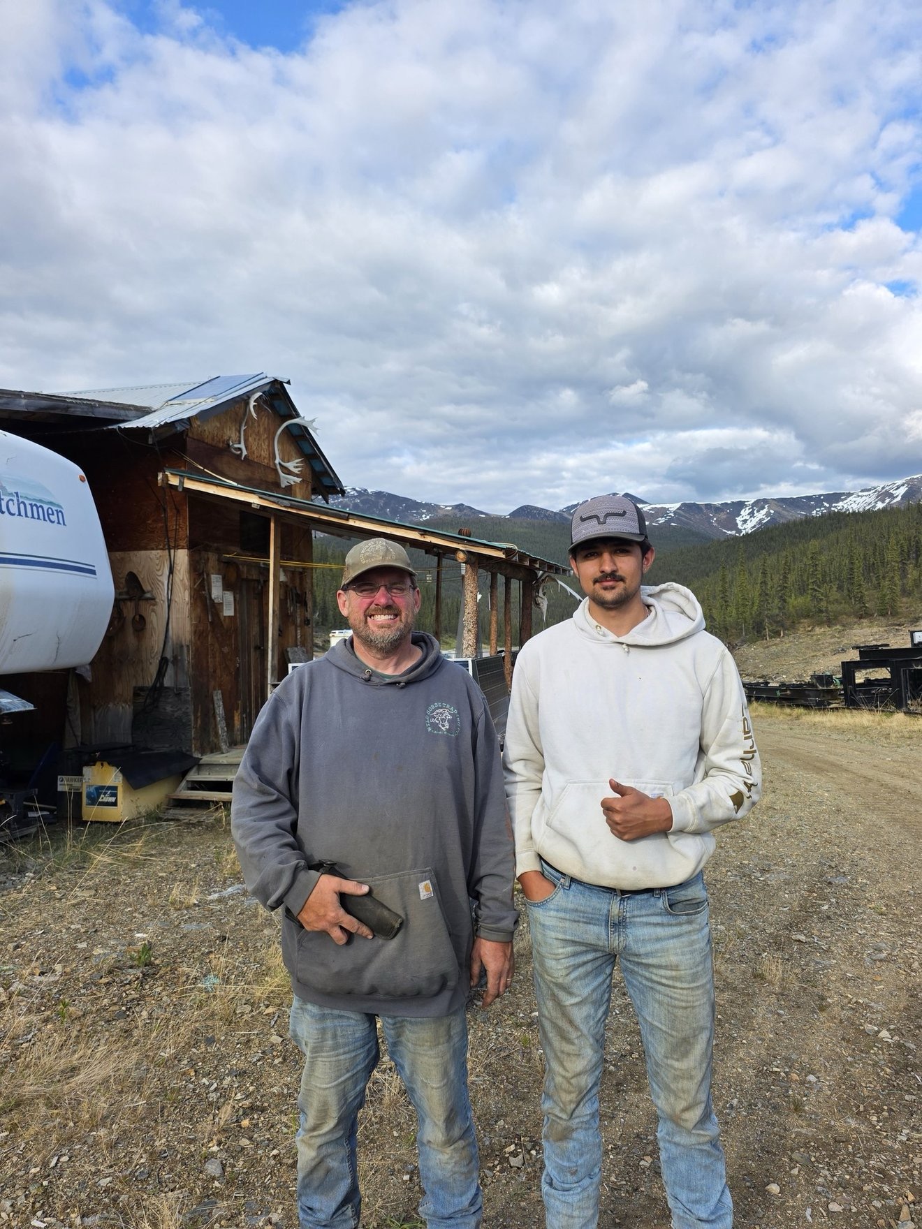 Two people posing outside a cabin at camp.