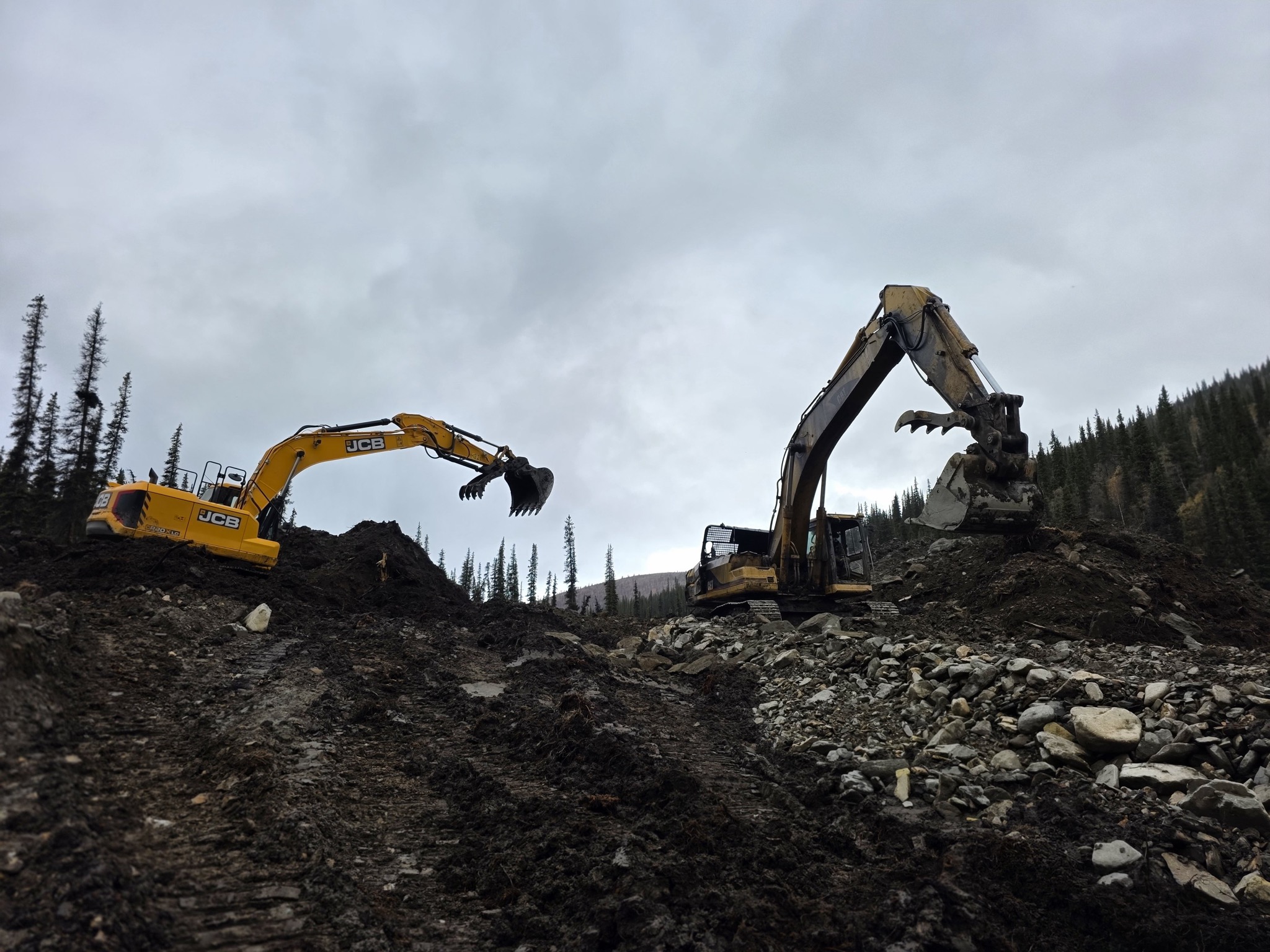 Two excavators working across a muddy placer cut.