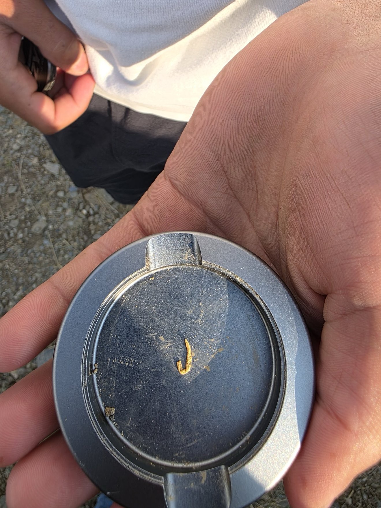 A small gold sample shown in a vial by hand.