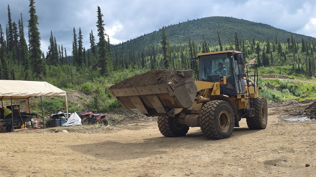 Loader carrying a full bucket of material across the claim.
